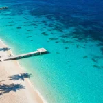 Aerial view of a turquoise Bahamas beach with palm trees and a wooden dock